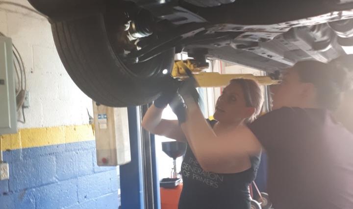 Two women working underneath a car